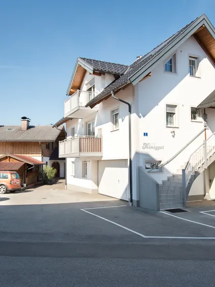 Modernes Gästehaus mit Balkonen und Parkplätzen davor an einem sonnigen Tag in Alpenregion