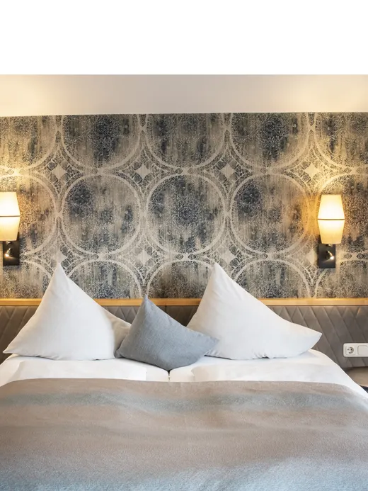 Modernes Hotelzimmer mit Doppelbett, geometrischer Tapete und sanfter Beleuchtung