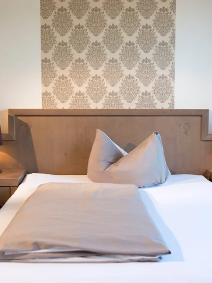 Modernes Hotelzimmer mit Holz-Doppelbett, Nachttischlampen und eleganter Tapete