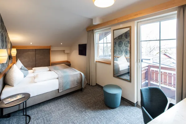 Modern hotel room with double bed, desk, balcony access and soft lighting
