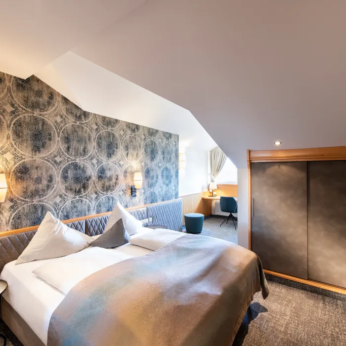 Modernes Hotelzimmer mit Doppelbett, gemusterter Wand, Schreibtisch und Einbauschrank