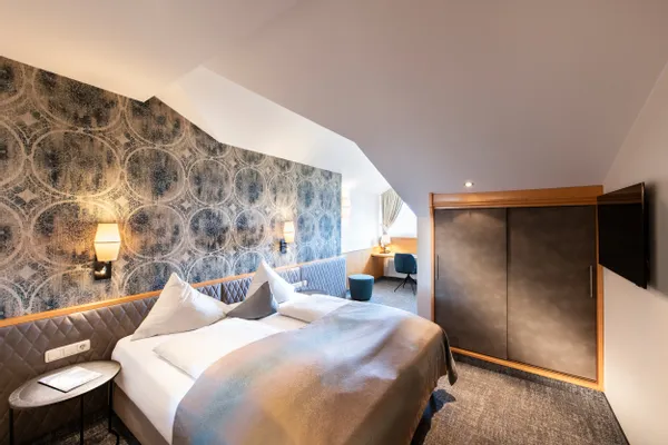 Modernes Hotelzimmer mit Doppelbett, gemusterter Wand, Schreibtisch und Einbauschrank