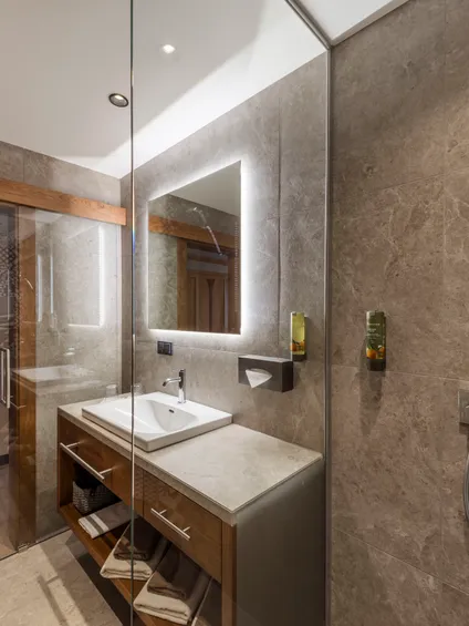 Modern bathroom with stone tiles, illuminated mirror, and walk-in shower