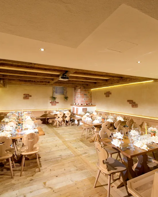 Rustikaler Speisesaal mit gedeckten Holztischen, Weinflaschen und warmer Beleuchtung