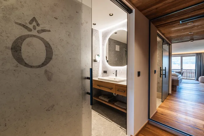 Modern hotel room with illuminated bathroom mirror and wooden floor leading to a balcony