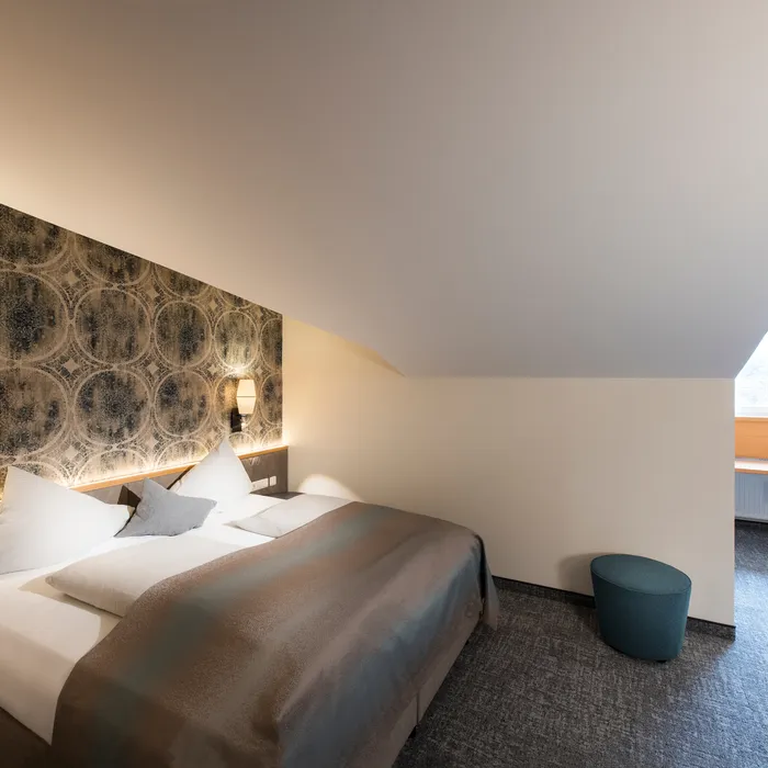 Modernes Hotelzimmer mit Doppelbett, stilvoller Tapete und Schreibtisch unter Dachschräge