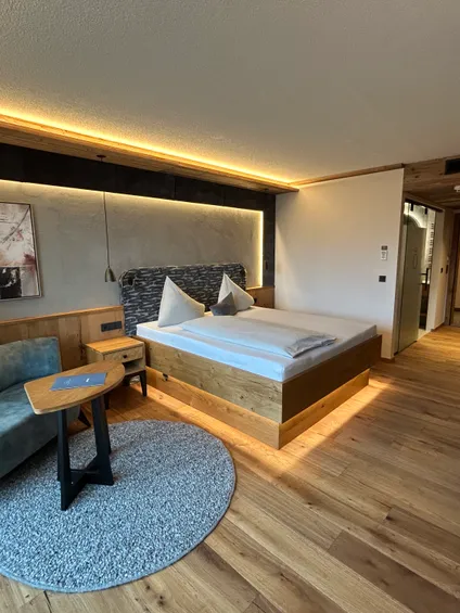 Modern hotel room with wooden flooring, double bed, sofa, and ambient lighting