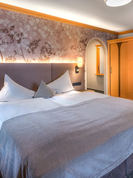 Gemütliches Hotelzimmer mit Doppelbett, Blumenwand und Kleiderschrank aus Holz