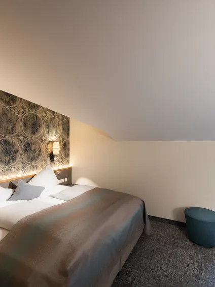 Modernes Hotelzimmer mit Doppelbett, stilvoller Tapete und Schreibtisch unter Dachschräge