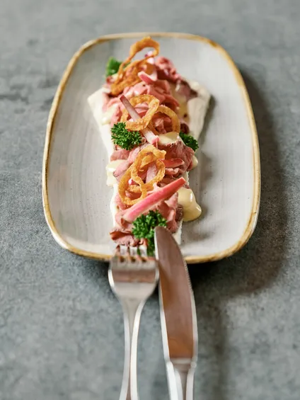 Traditioneller Rindfleischsalat mit Röstzwiebeln, Petersilie und Dressing auf Keramikteller
