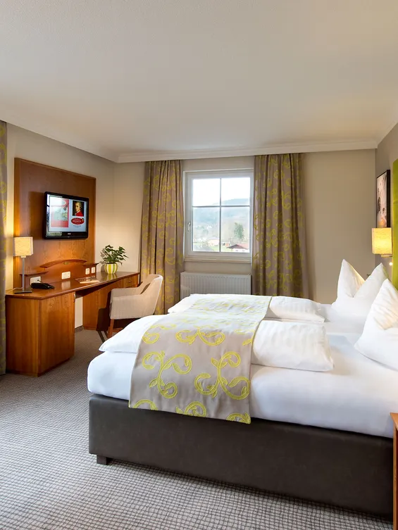 Modernes Hotelzimmer mit Doppelbett, grünem Kopfteil, Schreibtisch und Bergblick