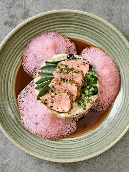 Filetto di maiale gourmet con schiuma rosa, purè di patate e erbe aromatiche su piatto di ceramica