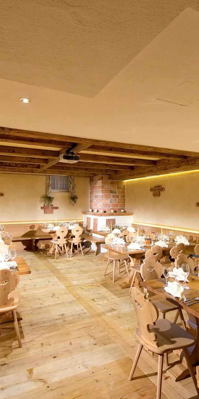 Rustikaler Speisesaal mit gedeckten Holztischen, Weinflaschen und warmer Beleuchtung