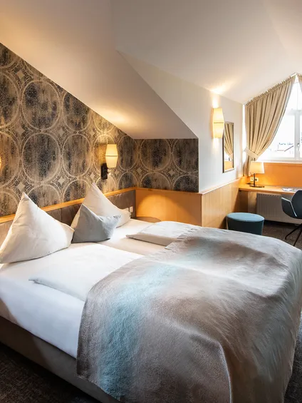 Camera d'hotel moderna con letto matrimoniale, soffitto inclinato, scrivania vicino alla finestra e TV a parete