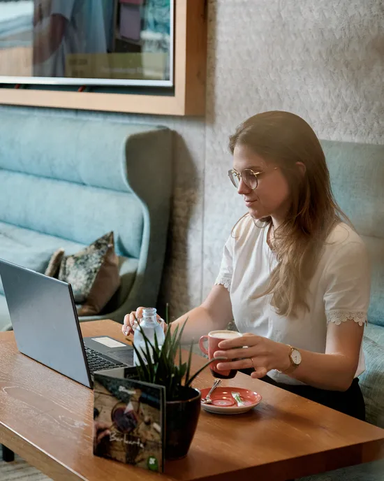 Woman working on laptop in cozy café with coffee and water on wooden table