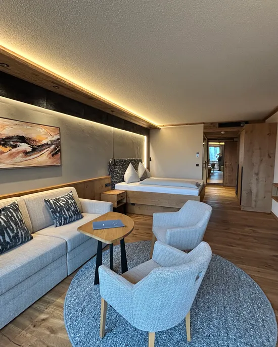 Modernes Hotelzimmer mit Doppelbett, Sofa, Sesseln, Holzboden und Ambientebeleuchtung
