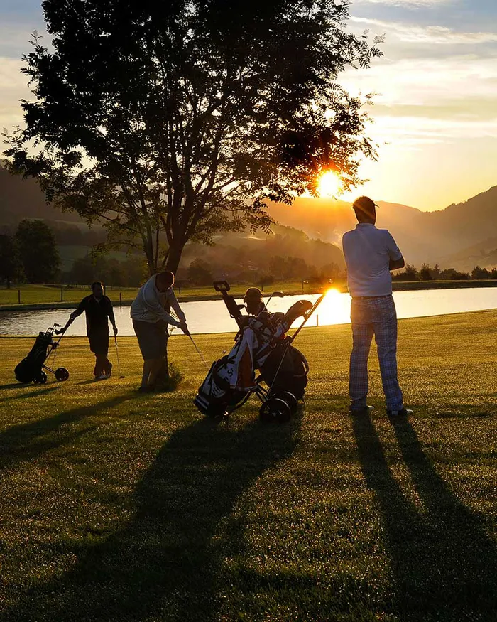 Golfspieler bei Sonnenuntergang neben einem See mit Bergblick im Hintergrund