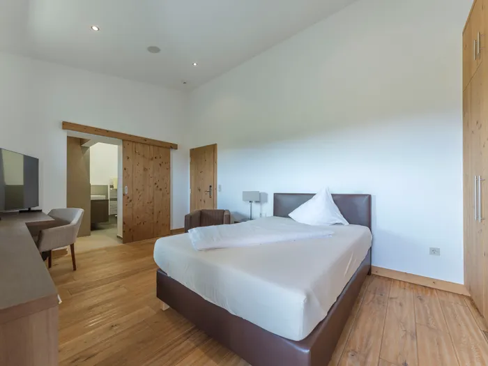 Modernes Hotelzimmer mit Holzboden, Doppelbett, Fernseher, Schreibtisch und Badezimmereingang