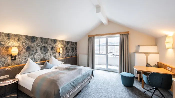 Modern hotel room with double bed, desk, balcony doors, and patterned accent wall