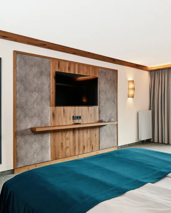 Modernes Hotelzimmer mit Doppelbett, TV-Wand aus Holz und Zugang zum Balkon