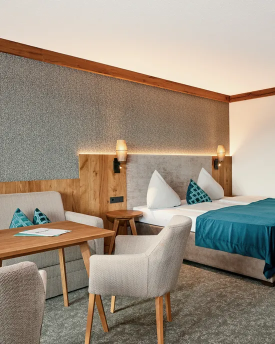 Modern hotel room with double bed, sofa, wooden table and teal accents