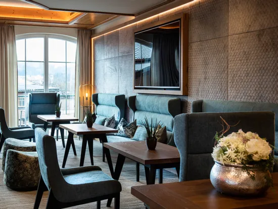 Moderne Hotellounge mit blauen Sesseln, Holztischen und großem Fenster mit Tageslicht