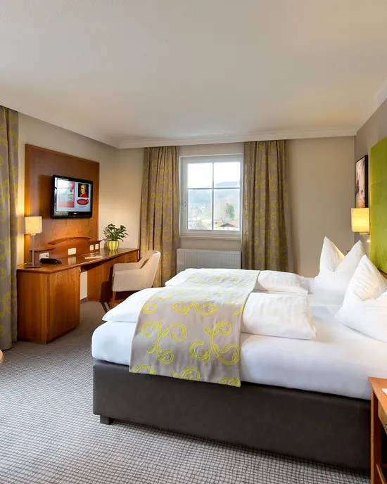 Modernes Hotelzimmer mit Doppelbett, grünem Kopfteil, Schreibtisch und Bergblick