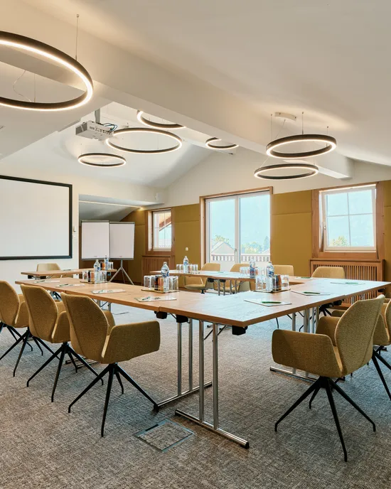 Moderner Konferenzraum mit U-förmigem Tisch, Beamerleinwand und runden Deckenleuchten
