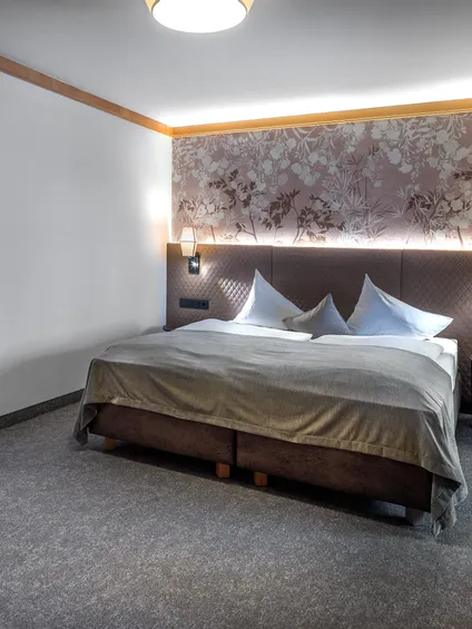 Gemütliches Hotelzimmer mit Doppelbett, floralem Kopfteil und sanfter Beleuchtung