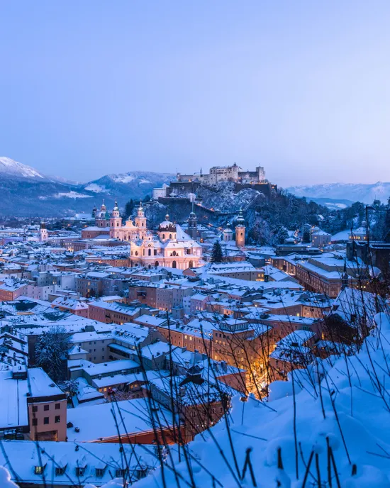 Winterblick auf Salzburgs Altstadt und Festung Hohensalzburg bei Dämmerung mit schneebedeckten Dächern