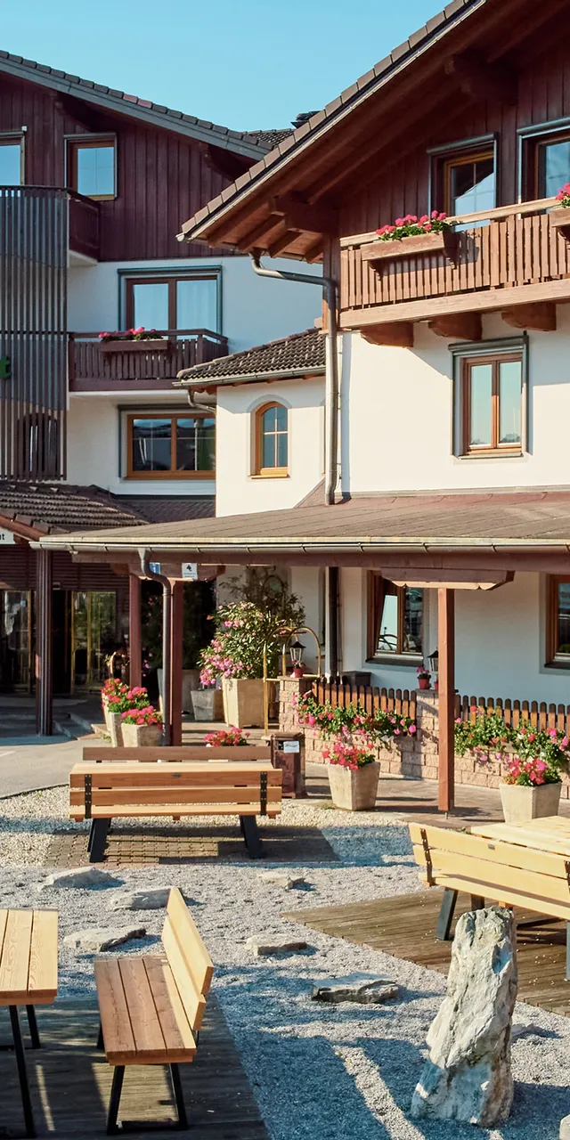 Traditionelles Alpenhotel mit Holzbalkonen, Sitzbereich im Freien und blühenden Pflanzen