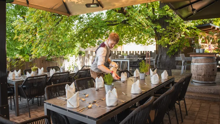 Kellner deckt Tisch im Außenbereich eines Restaurants unter Überdachung