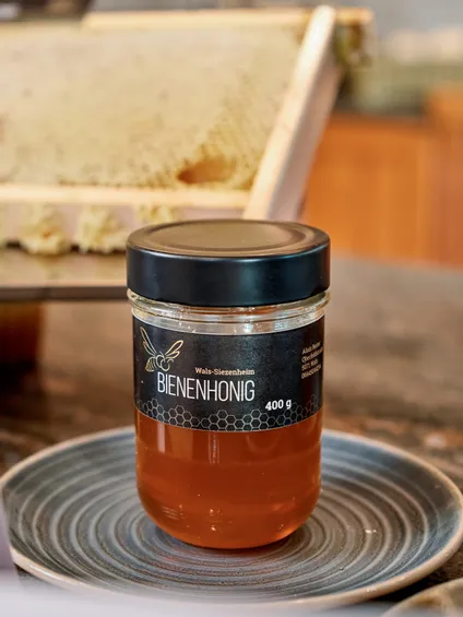 Glas mit 400 g Bienenhonig aus Wals-Siezenheim vor frischer Honigwabe auf einem Teller