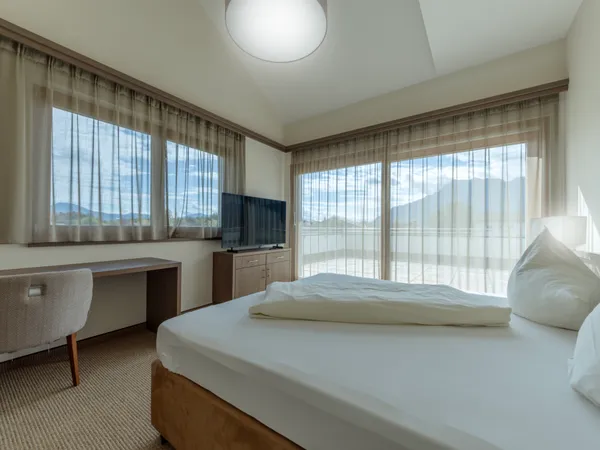 Bright hotel room with large windows, a bed, and a flat-screen TV