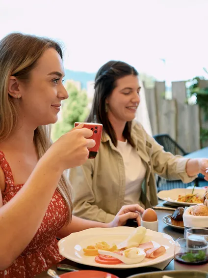 Zwei Frauen genießen Frühstück mit Kaffee, Brötchen und Käse auf einer Terrasse im Freien