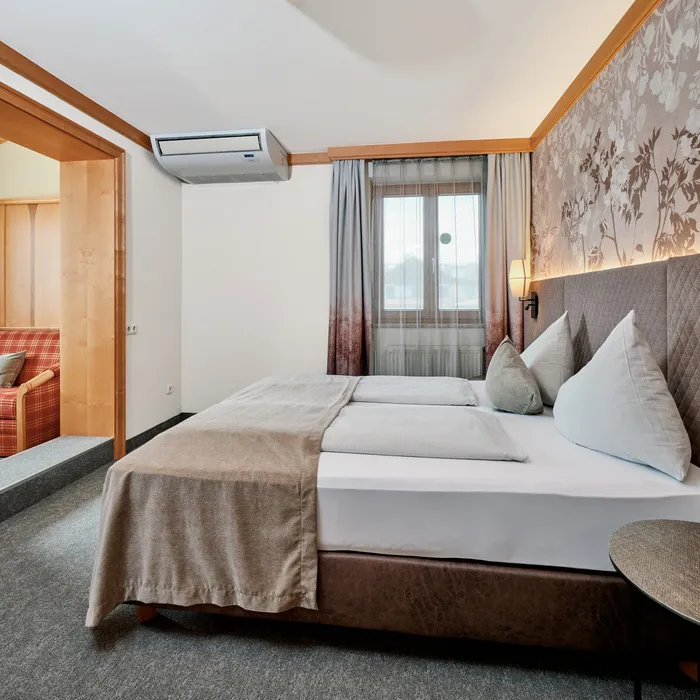Modernes Hotelzimmer mit Doppelbett, floraler Akzentwand und Blick in gemütlichen Sitzbereich