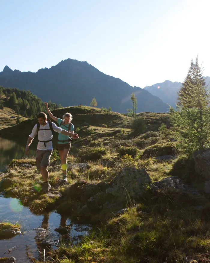 Coppia in escursione tra paesaggi alpini vicino a un lago di montagna al sole