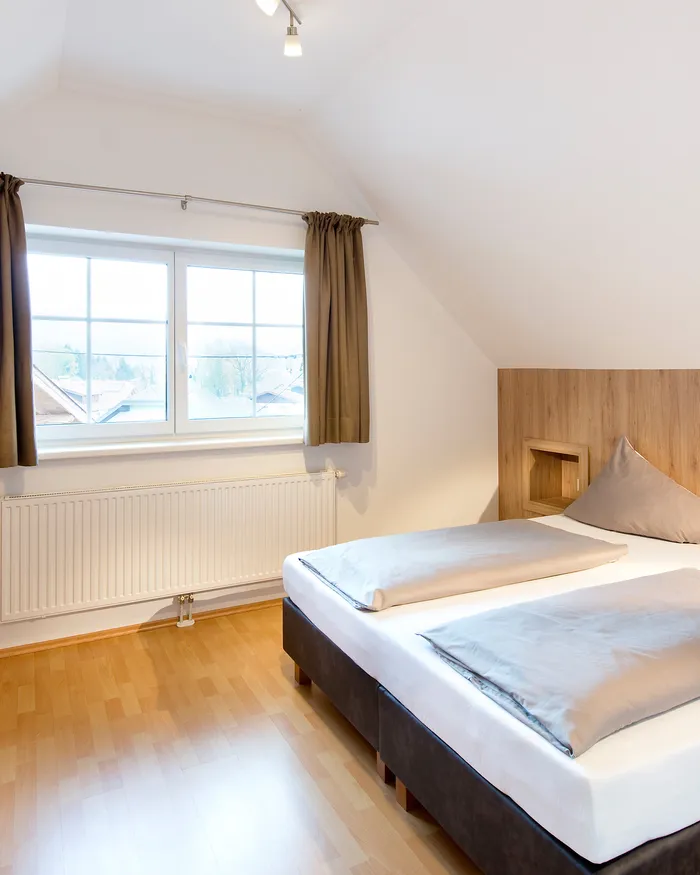 Modernes Dachgeschoss-Schlafzimmer mit Doppelbett, Holzmöbeln und schräger Decke
