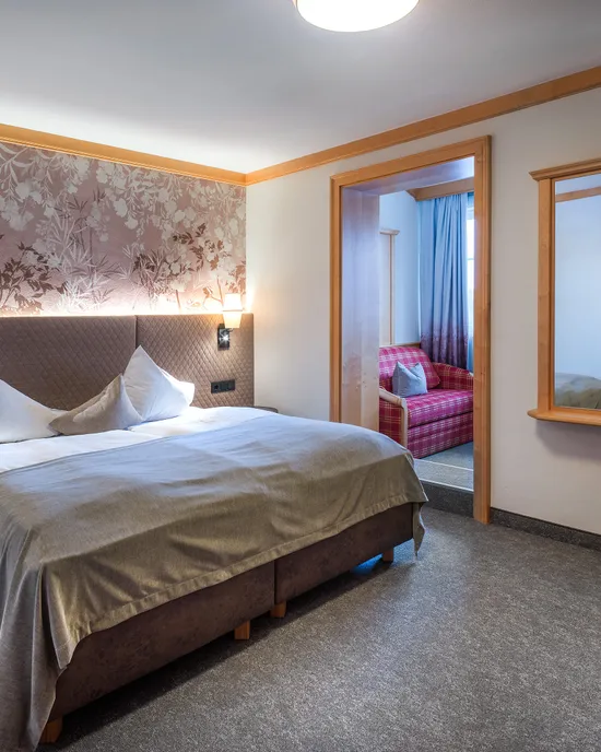 Cozy hotel room with double bed, floral headboard, wall sconces and adjoining seating area