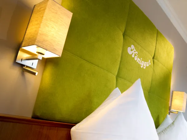 Hotel bed with green padded headboard and soft lighting at Königgut
