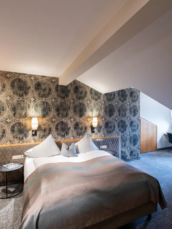 Modernes Hotelzimmer mit Doppelbett, gemusterter Tapete, Schreibtisch und gemütlicher Beleuchtung