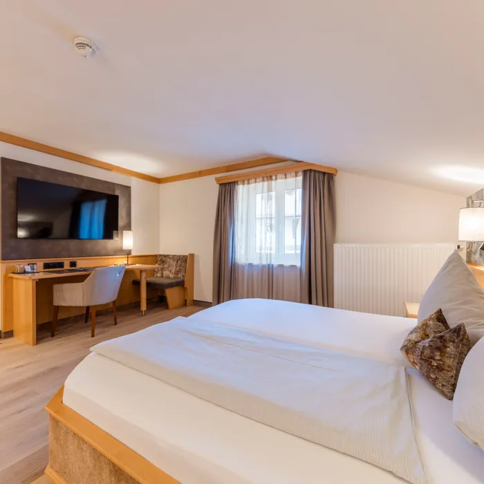 Gemütliches Hotelzimmer mit Doppelbett, Schreibtisch, großem Fernseher und Vorhängen