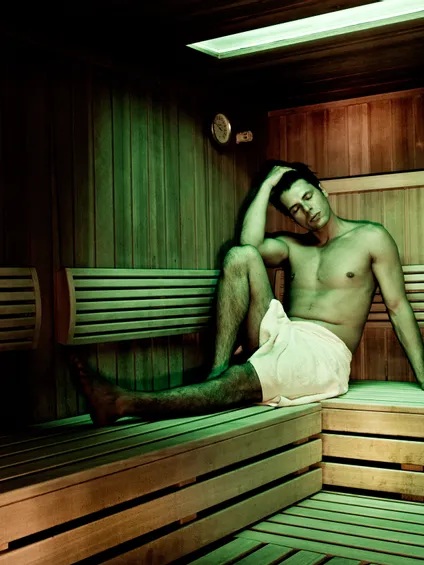 Uomo che si rilassa in una sauna di legno con asciugamano sotto luce verde soffusa
