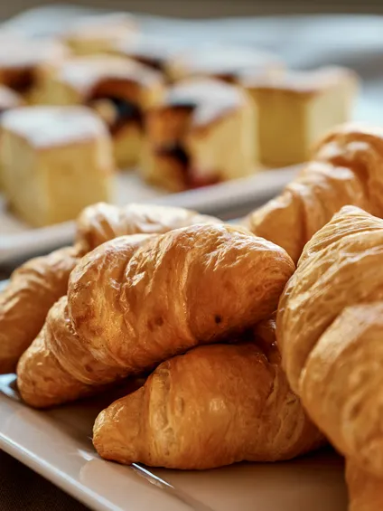 Frische Croissants auf weißem Teller mit Gebäckstücken im Hintergrund
