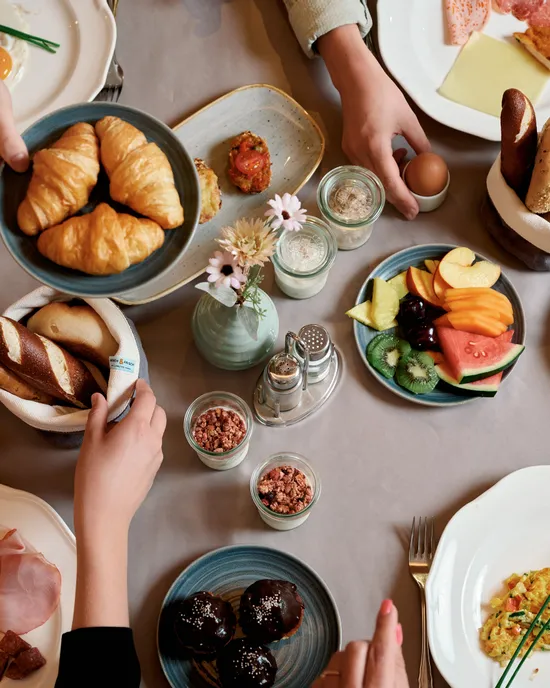 Brunch-Tisch mit Croissants, Obst, Käse, Brot, Eiern, Kaffee und verschiedenen Frühstücksgerichten