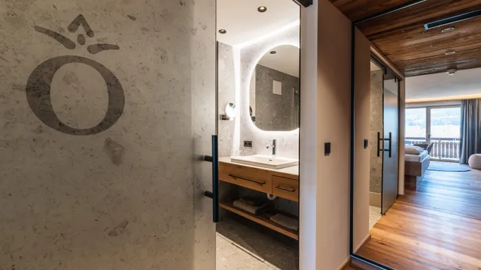 Modern hotel room with illuminated bathroom mirror and wooden floor leading to a balcony