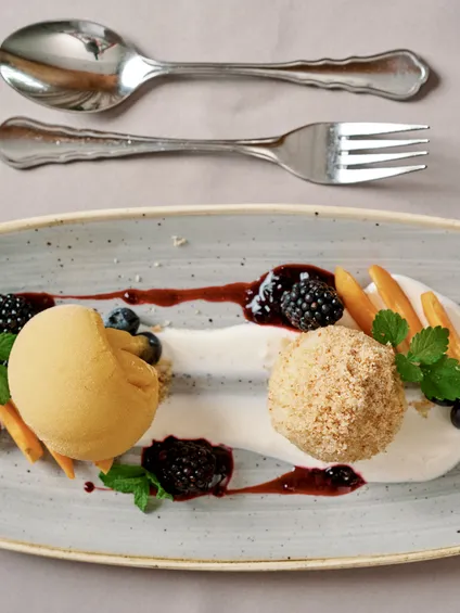 Gourmet-Dessert mit Eis, Früchten, Bröseln und Beerensauce auf Keramikteller
