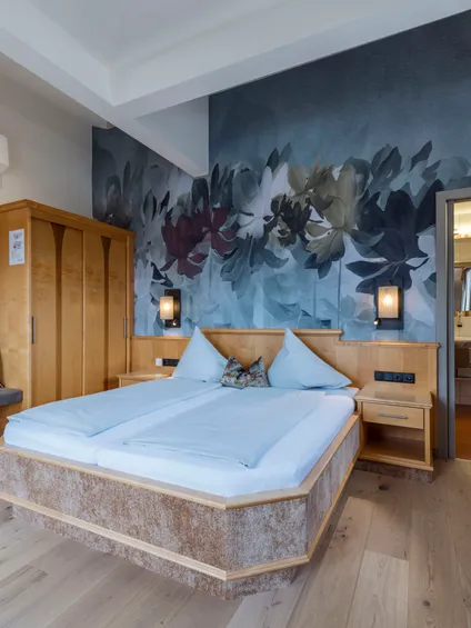 Hotelzimmer mit moderner Einrichtung, Holzboden, großem Bett, Blumenwandbild und eigenem Bad