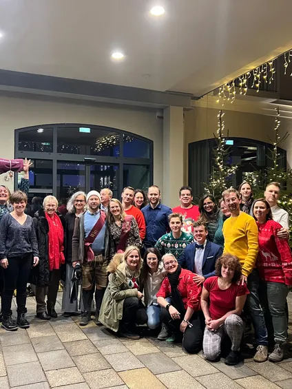 Gruppe von Menschen feiert Weihnachten draußen mit Lichtern und geschmückten Bäumen