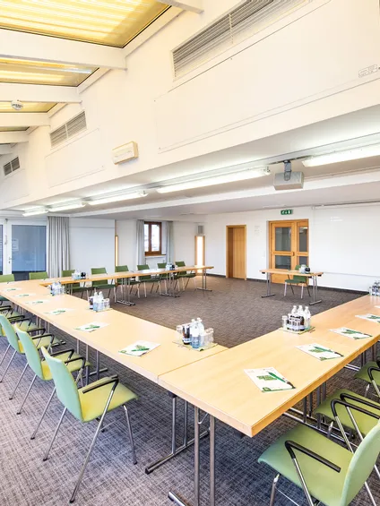 Heller moderner Konferenzraum mit U-förmiger Tischanordnung, grünen Stühlen und Mineralwasser